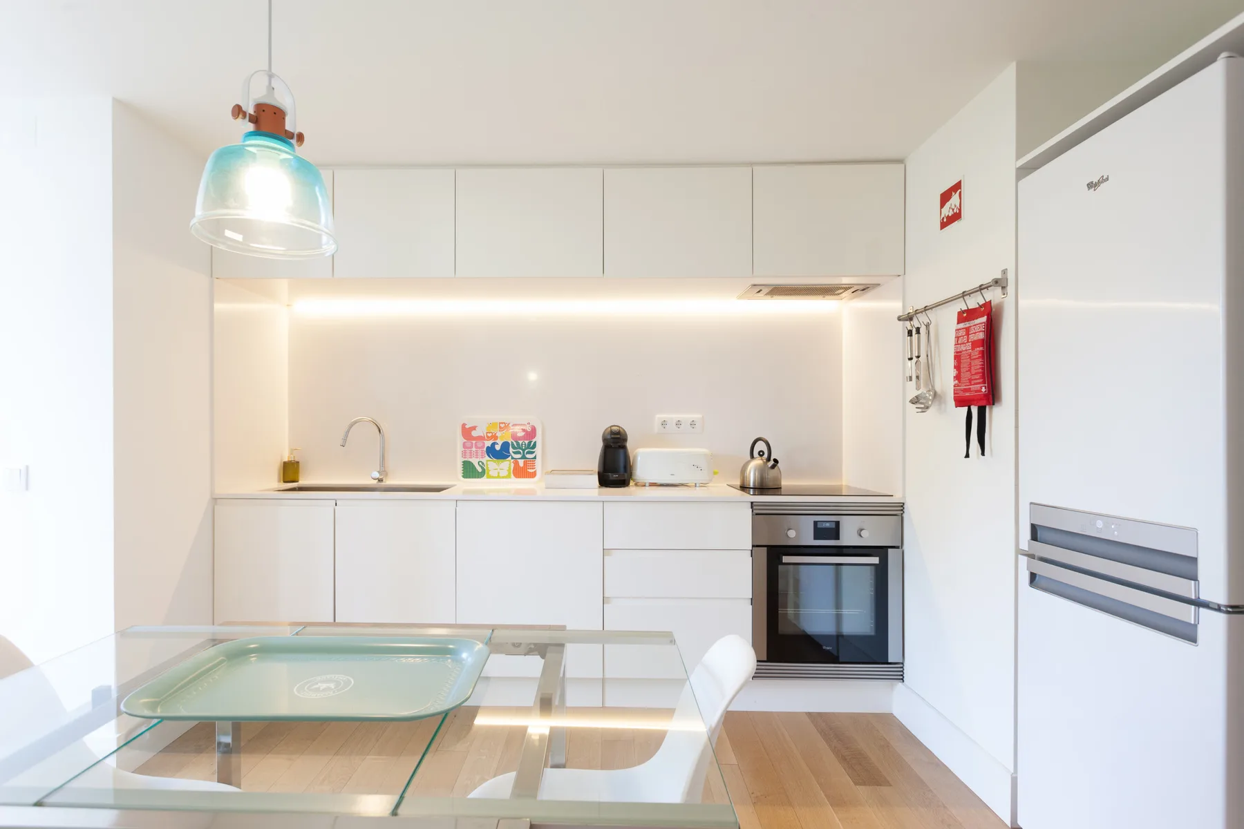 A bright kitchen with white cabinets and a glass dining table.