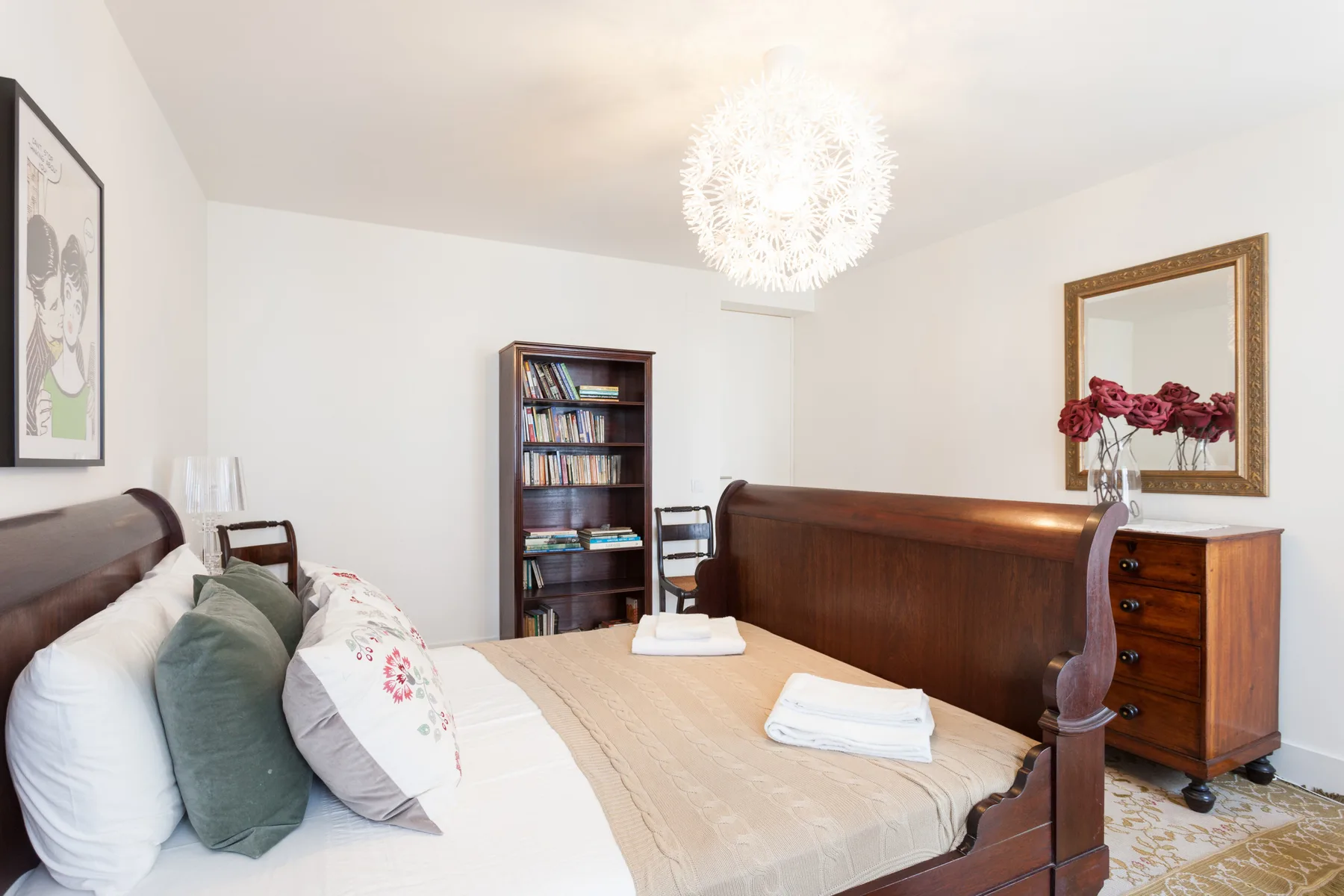 A bedroom with a wooden bed, folded towels, and a bookcase.