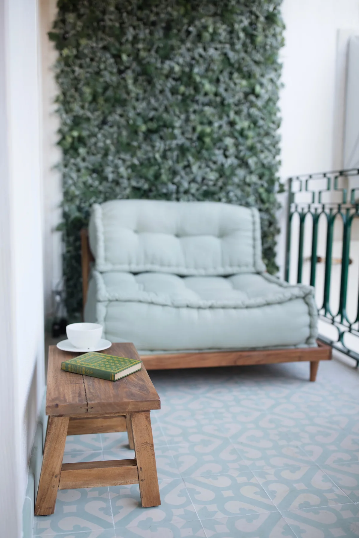 A small seating area with a cushioned bench, wooden table, and leafy wall.