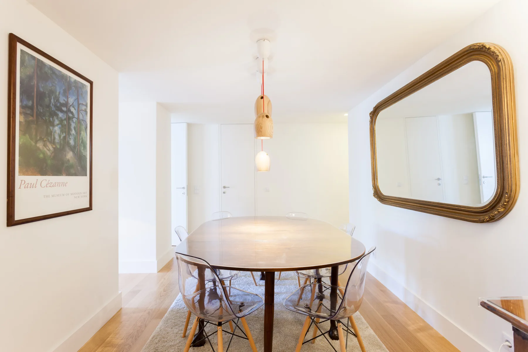 A bright dining area with an oval table, clear chairs, and a wall mirror.