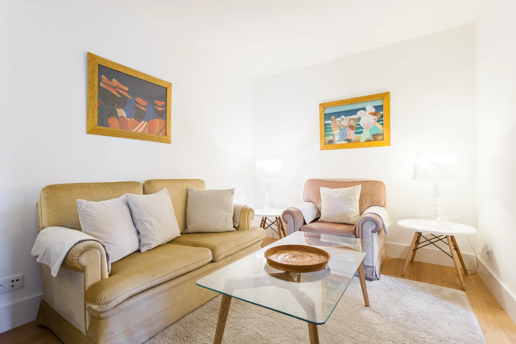 A bright living room with seating, a glass coffee table, and framed artwork.