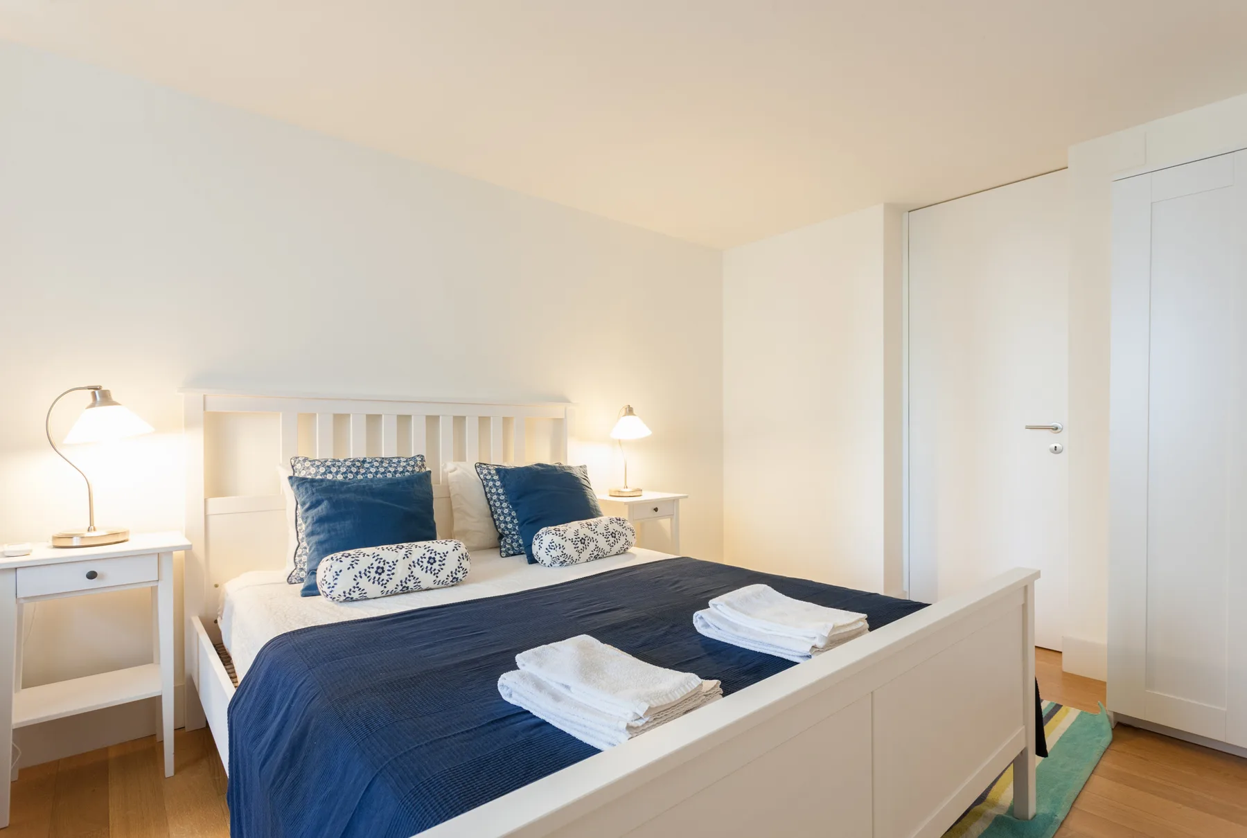 A bedroom with a double bed, blue bedding, and folded towels.