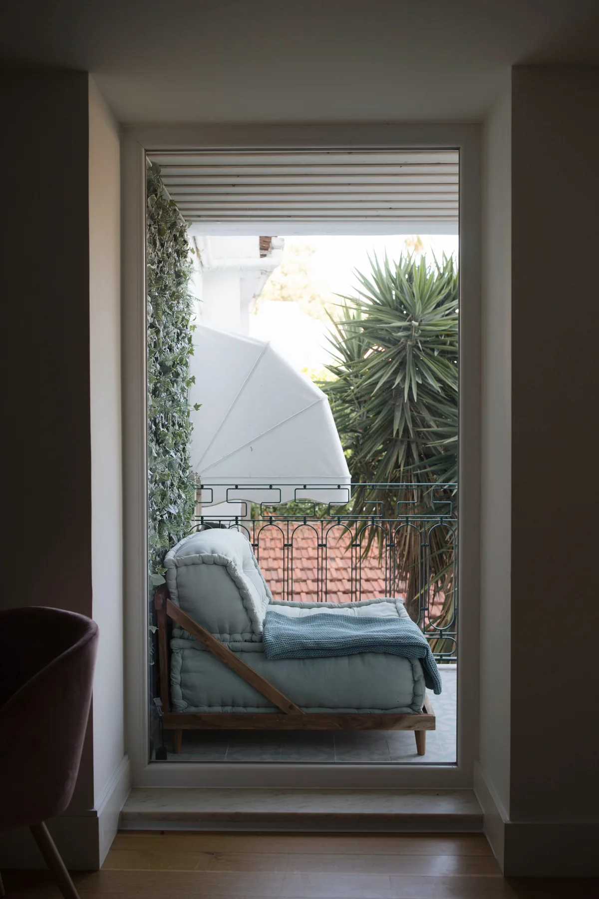 A doorway opens onto an outdoor seating area with a cushioned lounge chair and plants.