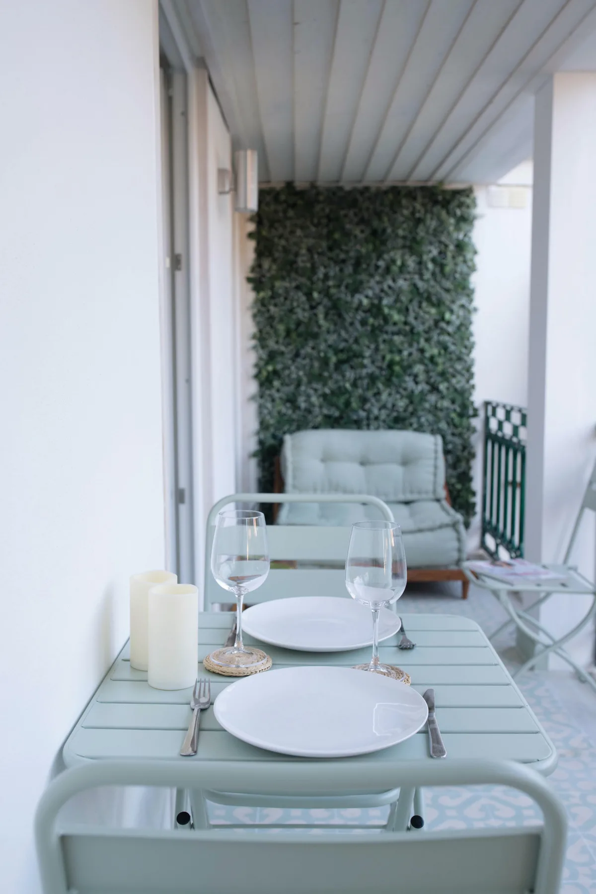 A covered terrace with a set dining table and leafy wall.
