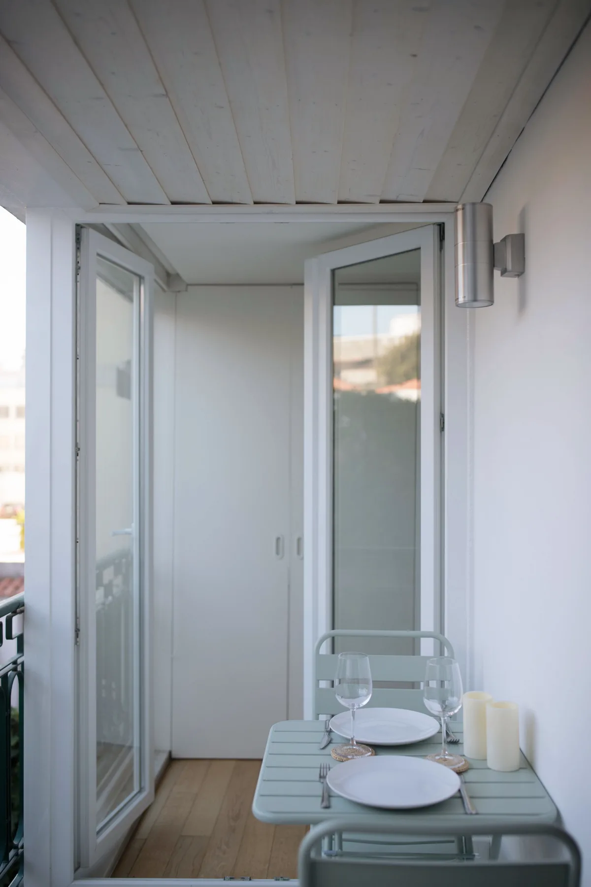A small outdoor terrace has a table set with plates beside open glass doors.