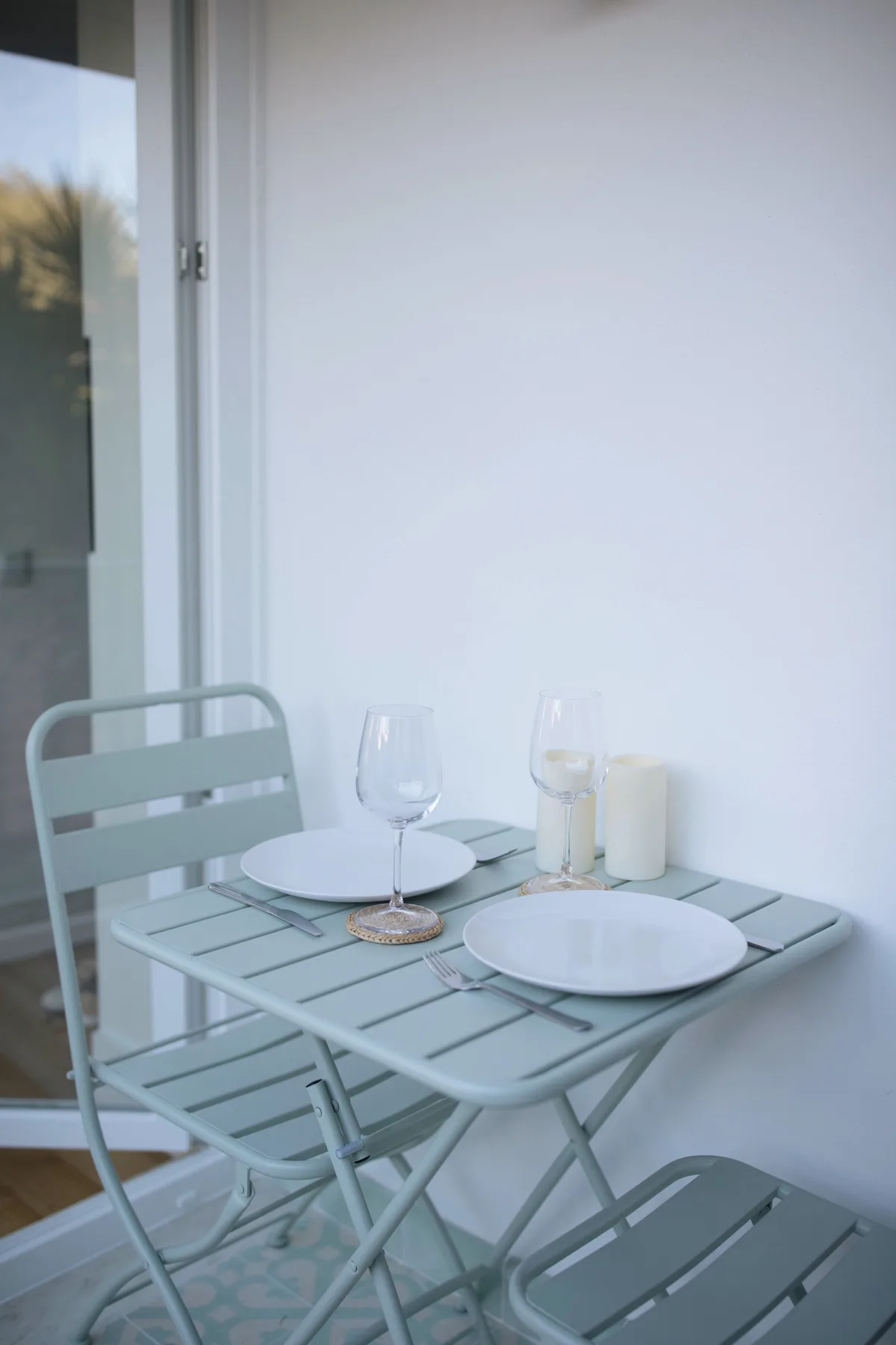 A small outdoor dining area has a metal table set with plates and glasses.