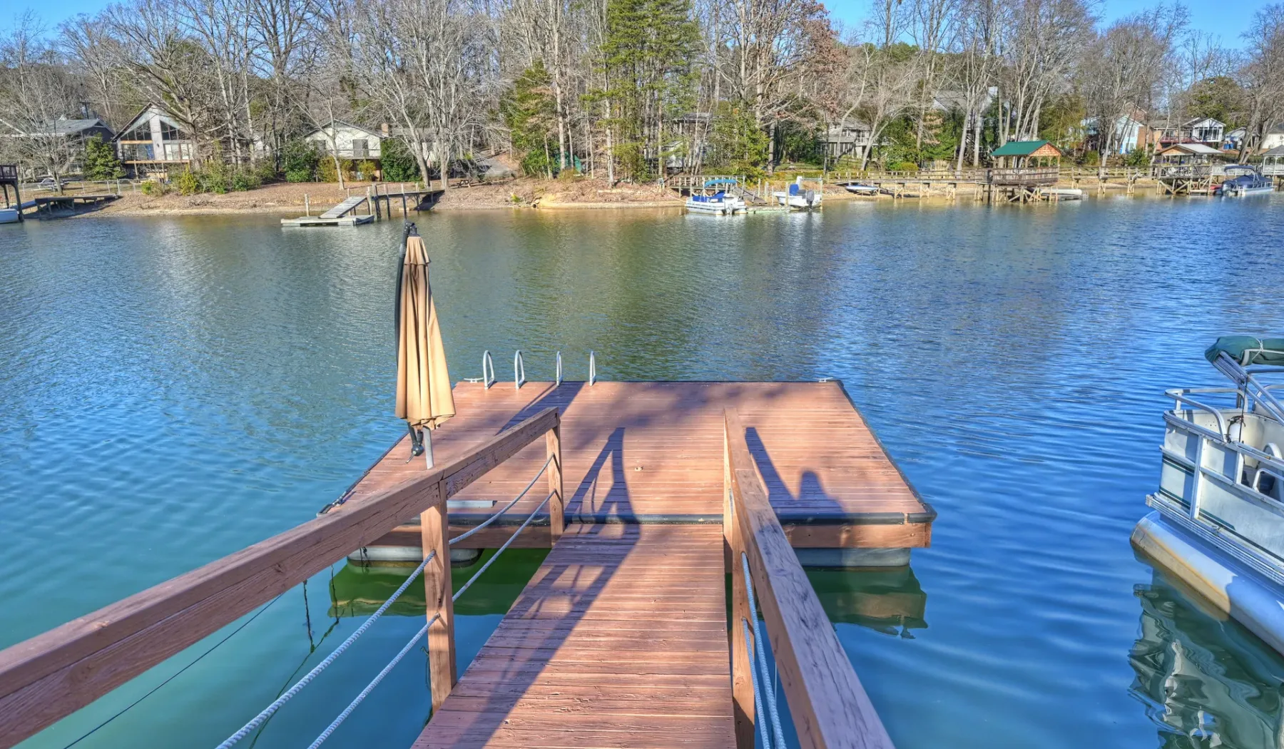 Un muelle de madera se adentra en un lago, con embarcaciones en la orilla opuesta.