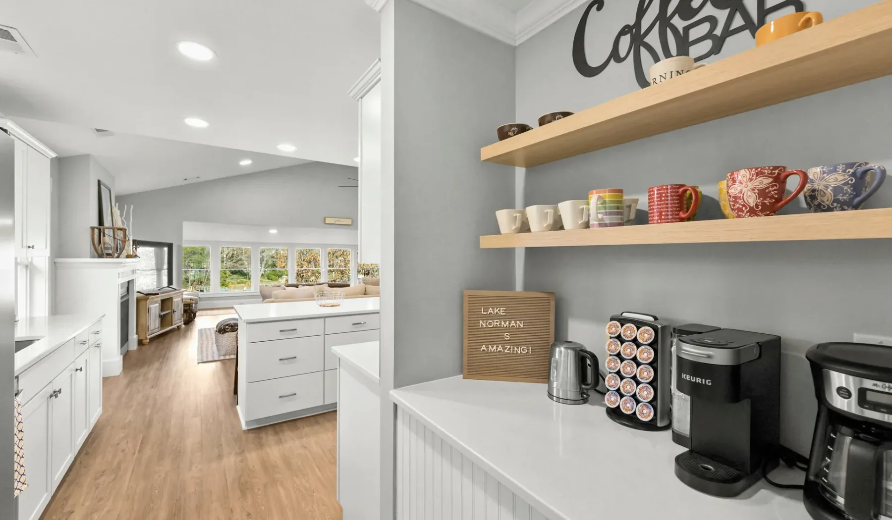 Una encimera de cocina con cafeteras está junto a una cocina abierta y comedor.