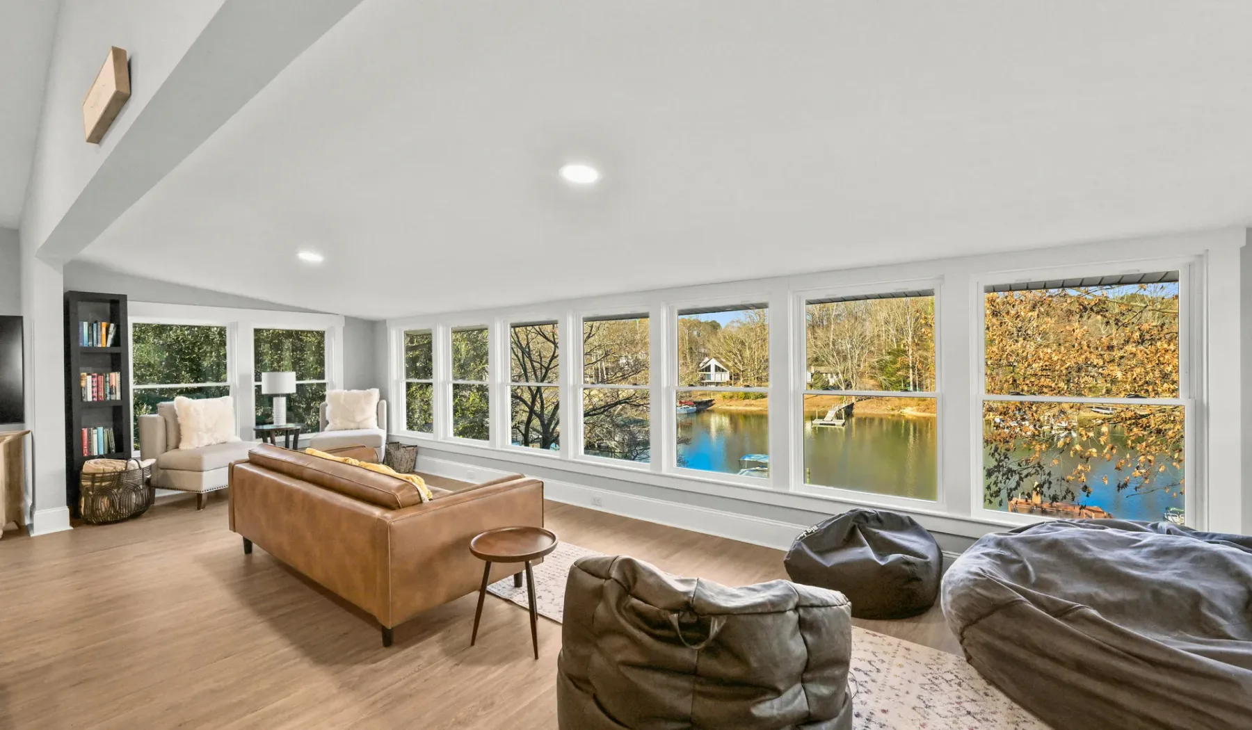 Una sala luminosa tiene grandes ventanas con vistas a árboles y agua.