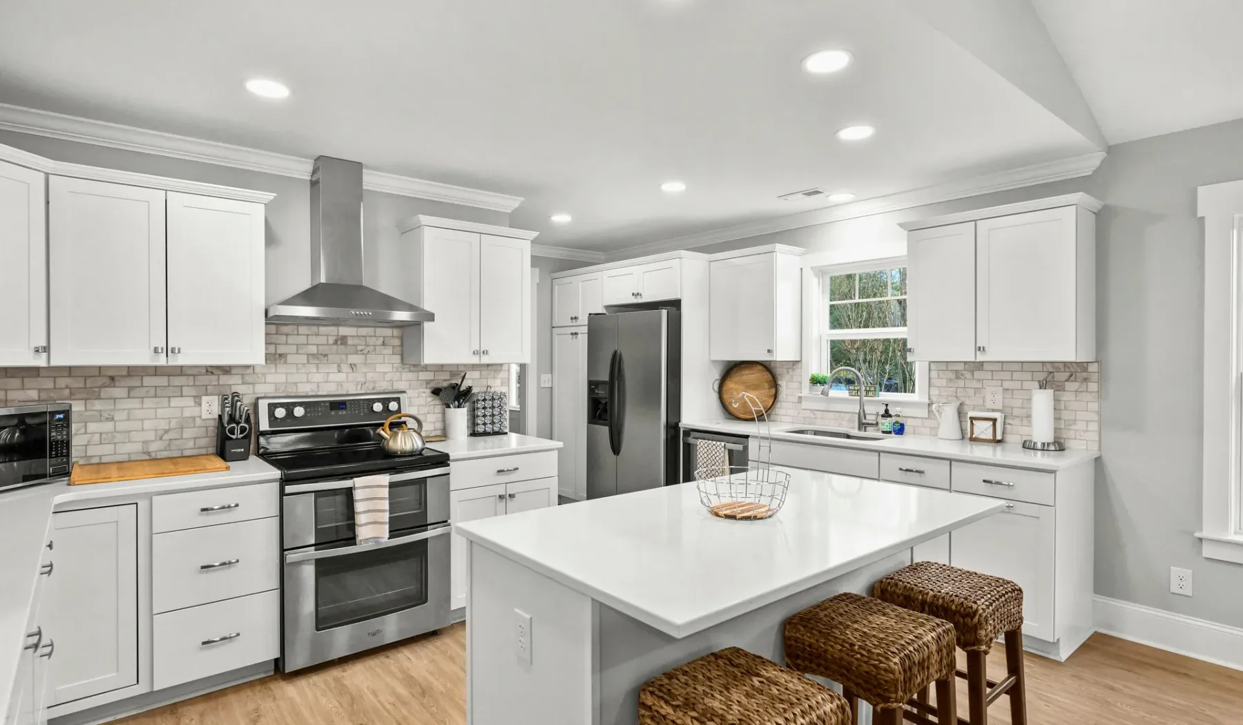 Una cocina luminosa con gabinetes blancos, electrodomésticos de acero inoxidable y una isla central.