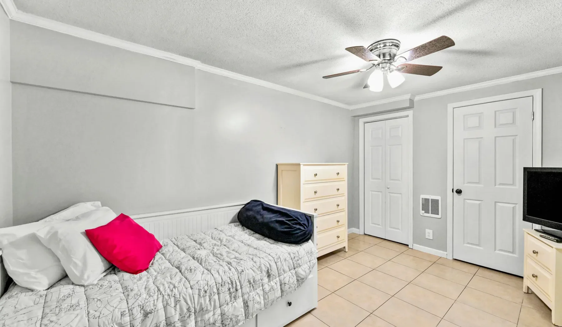 Un dormitorio con una cama, ropa de cama clara, una cómoda y dos puertas.