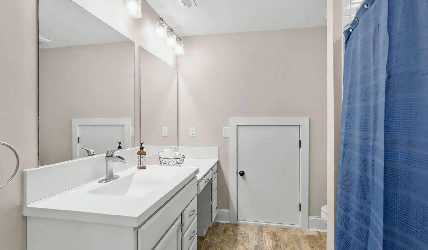 Un lavabo de baño está junto a una puerta cerrada y una cortina de ducha azul.