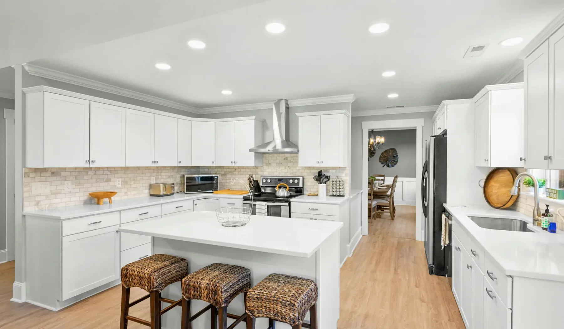 Una cocina luminosa con gabinetes blancos, una isla central y piso de madera.