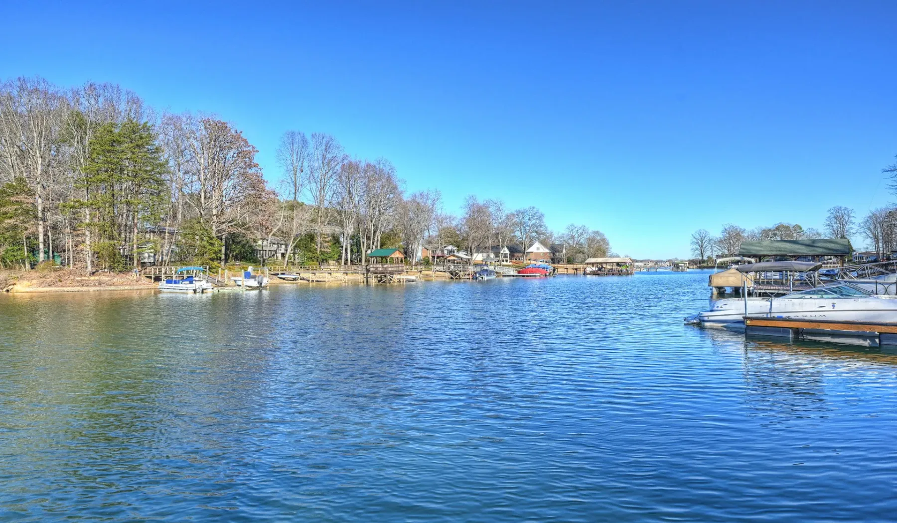 Escena junto a un lago, con embarcaciones y muelles en una orilla arbolada.