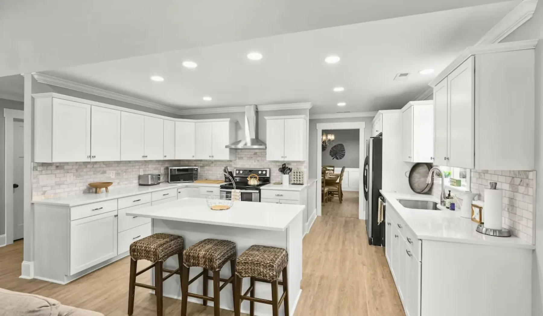 Una cocina luminosa con gabinetes blancos, una isla central y asientos de bar.