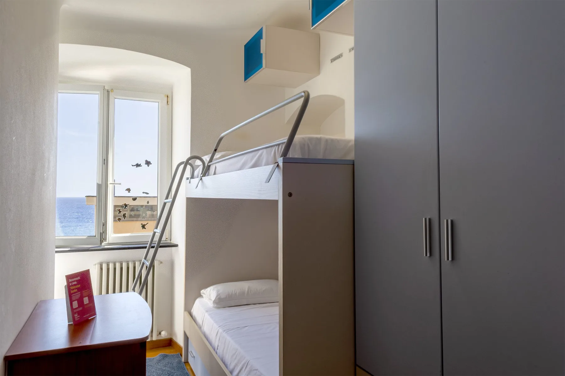 Un dormitorio compacto tiene literas junto a un armario alto y una ventana con vista al agua.