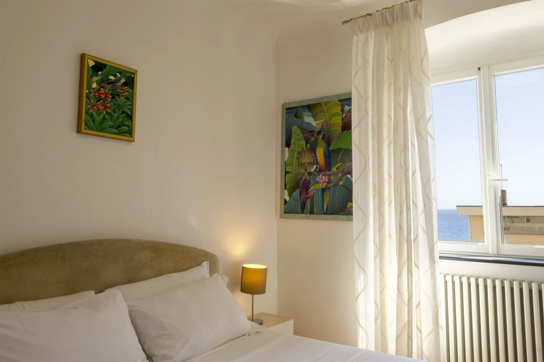 Un dormitorio con una cama junto a una ventana y cortinas claras.