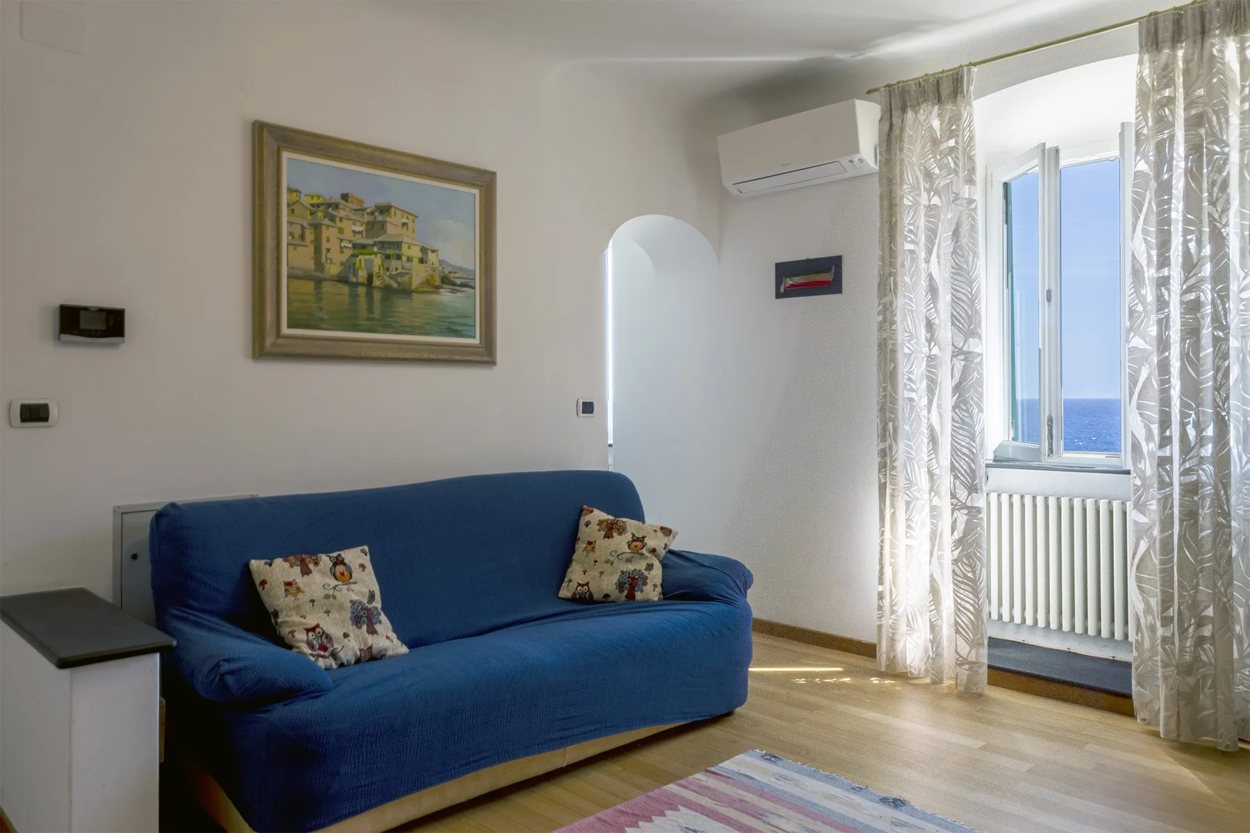 Una sala luminosa con asientos azules junto a una ventana con cortinas y vista al agua.