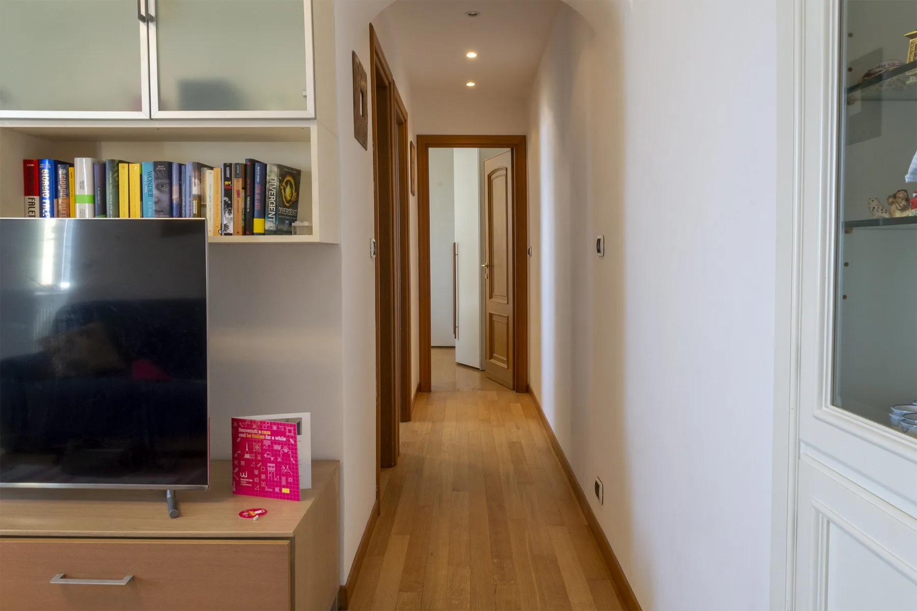 Un pasillo con suelo de madera pasa junto a un televisor y estanterías empotradas.