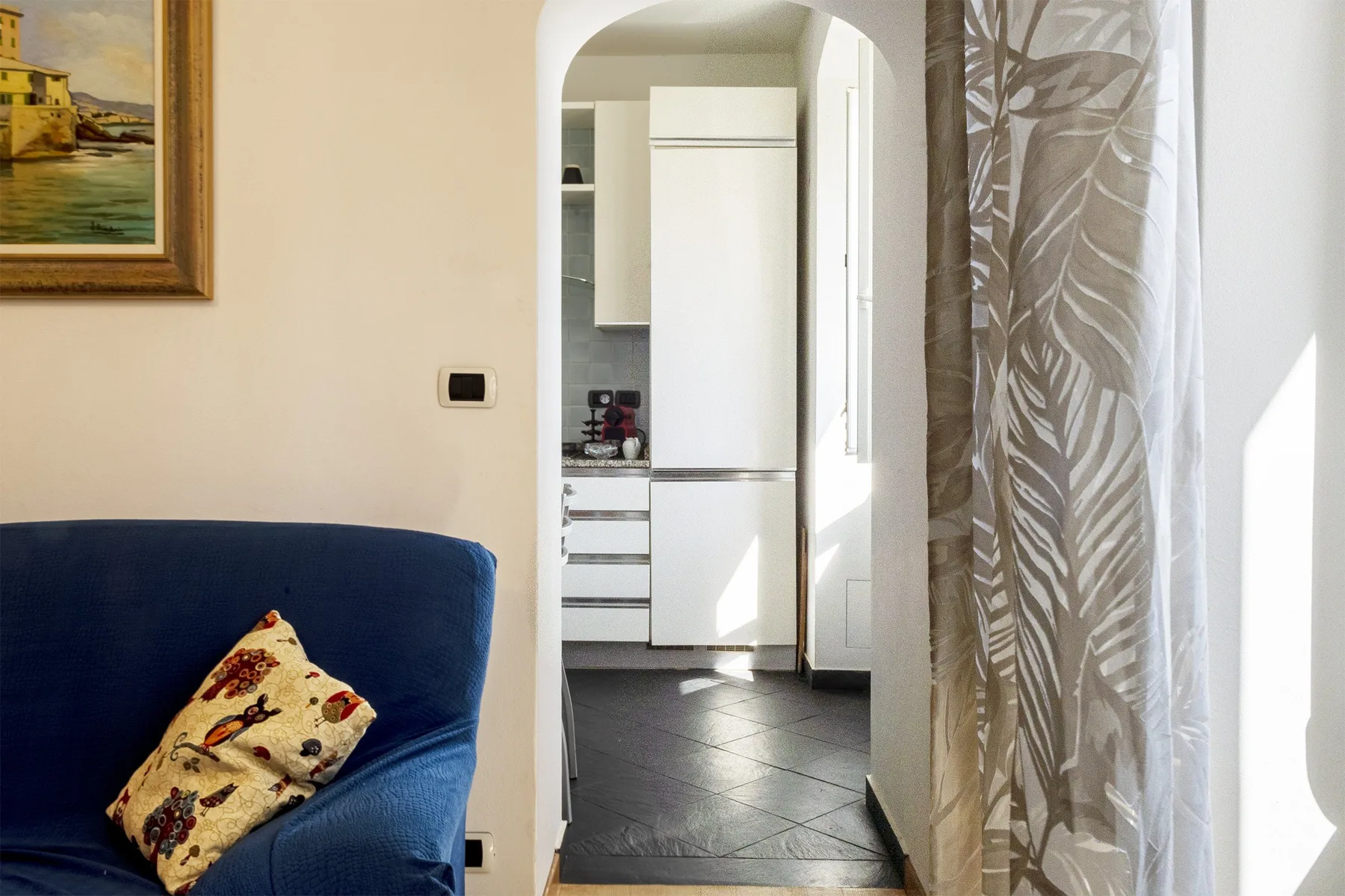 Una sala de estar con asientos azules junto a un arco que da a la cocina.
