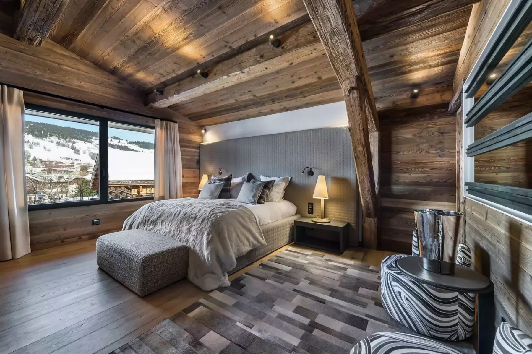 A bedroom with a large bed, bedside tables, and a window overlooking a snowy landscape.