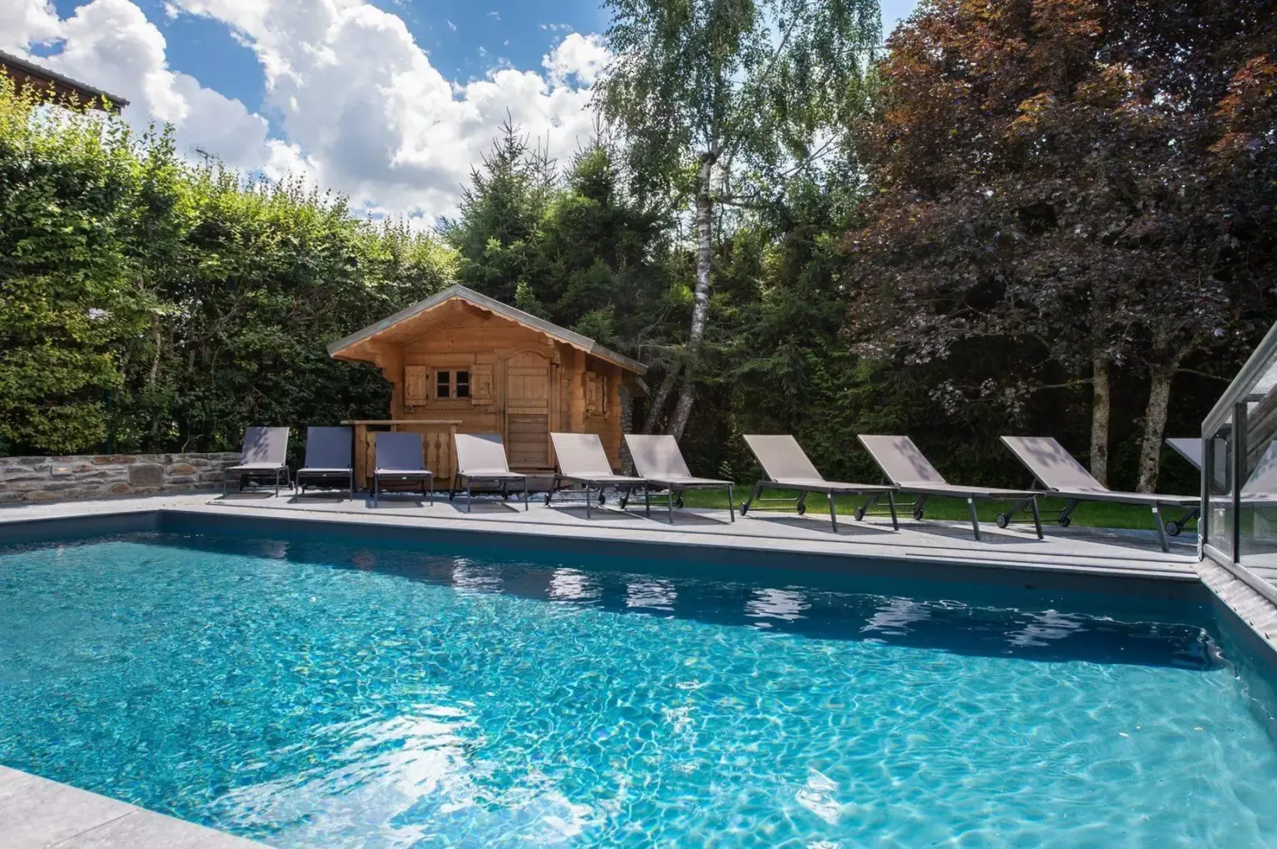 An outdoor swimming pool with lounge chairs and a wooden shed beside it.
