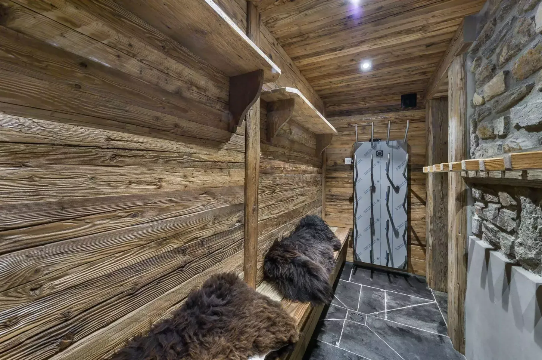 A rustic wooden sauna interior with a bench and stone flooring.