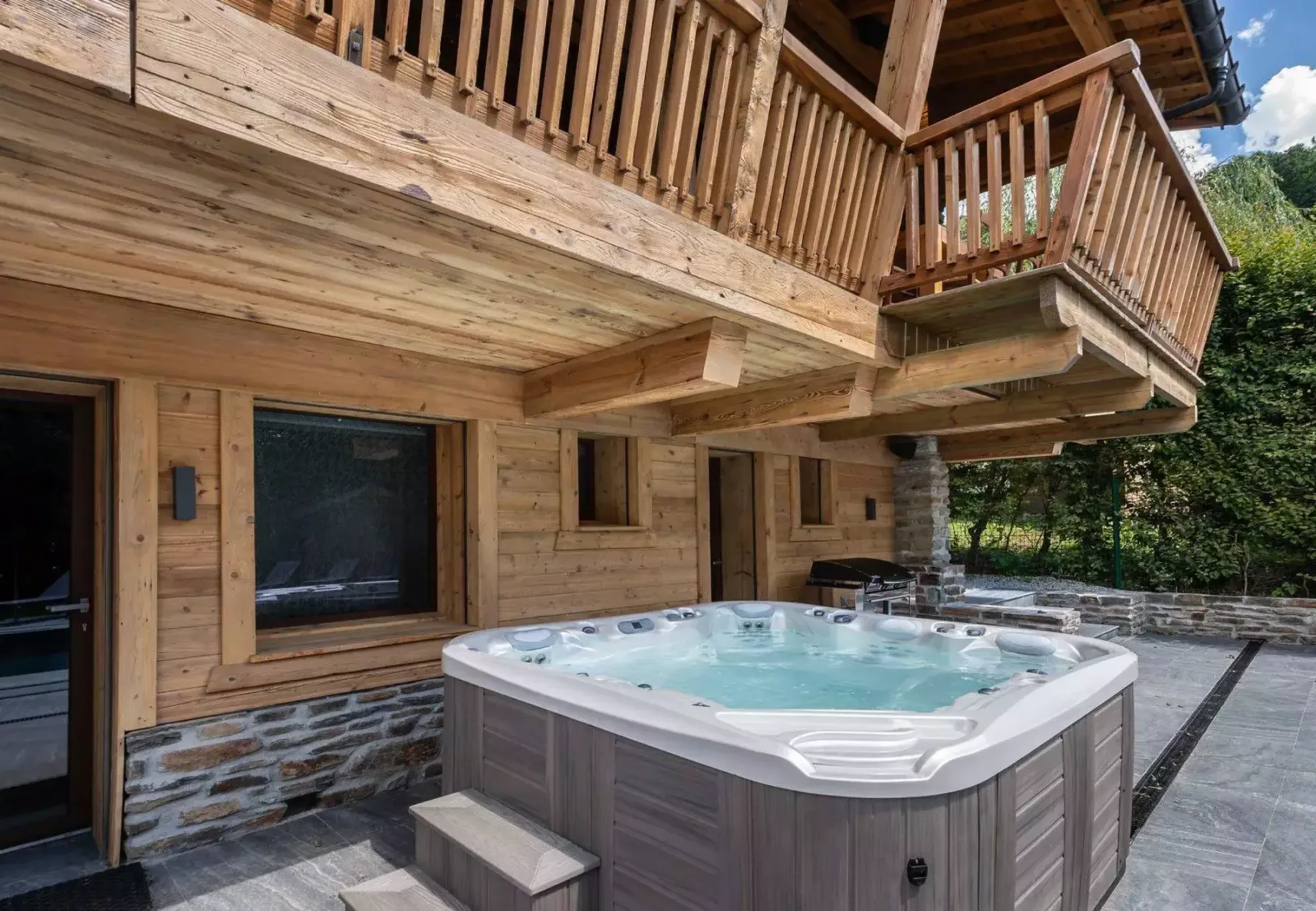Bañera de hidromasaje al aire libre junto a un chalet de madera con balcón encima.