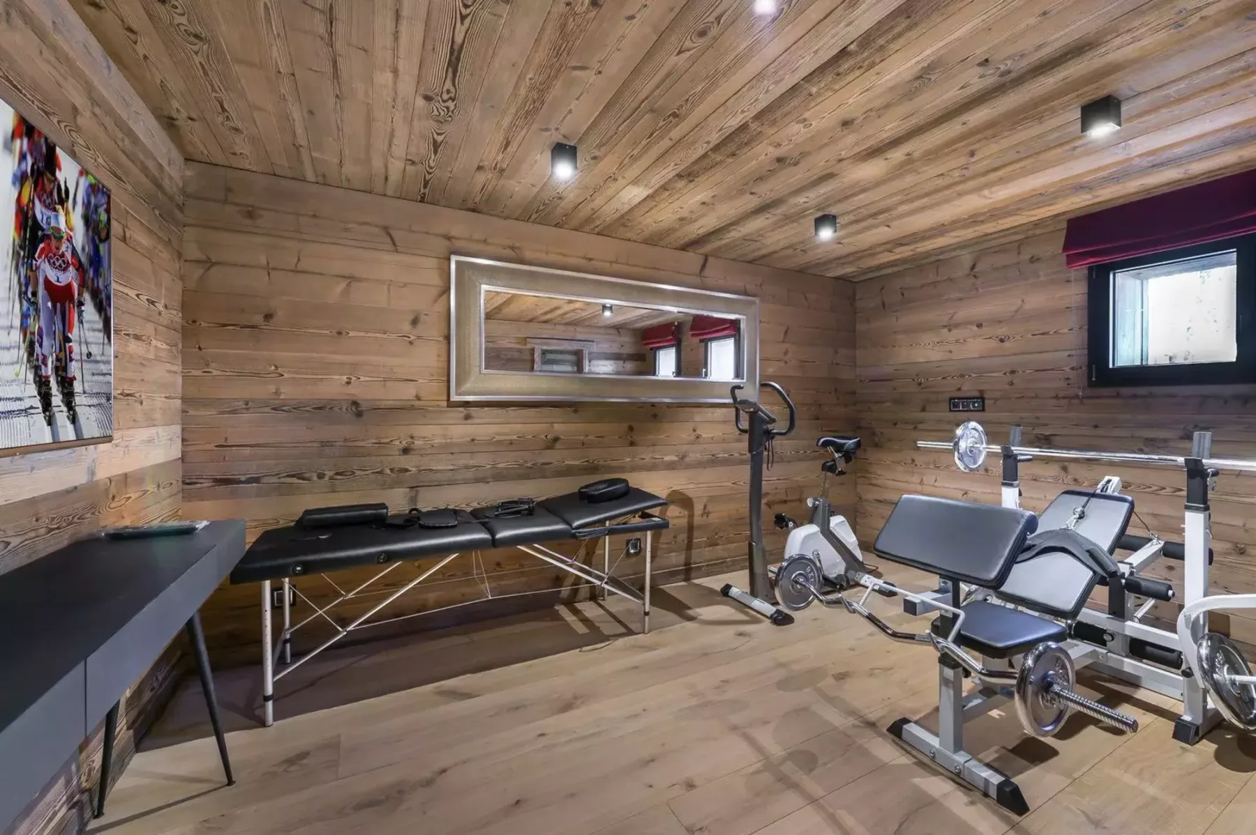 A wood-paneled fitness room with exercise equipment and a treatment table.