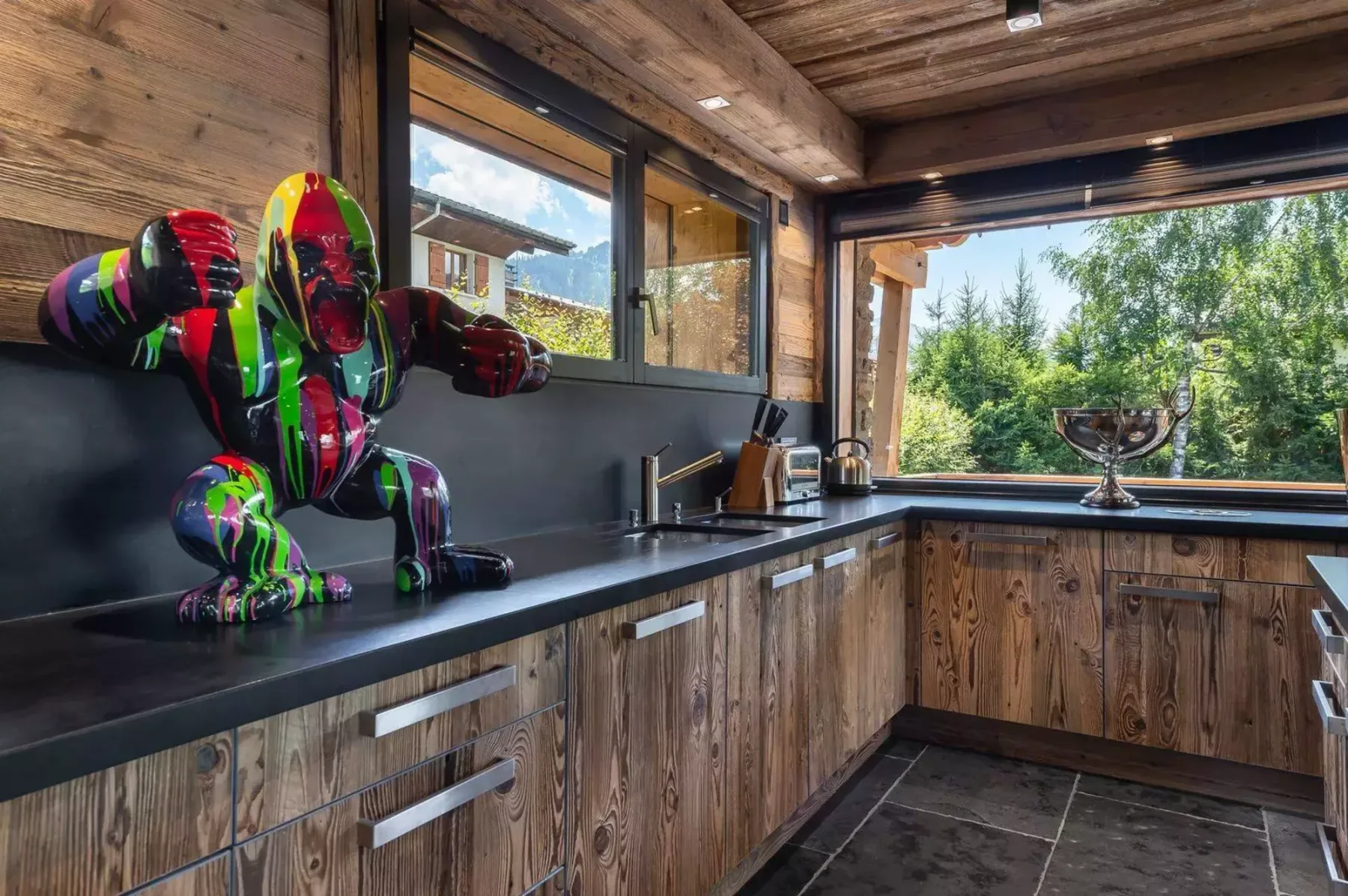 A wood-paneled kitchen with dark countertops and large windows overlooking greenery.