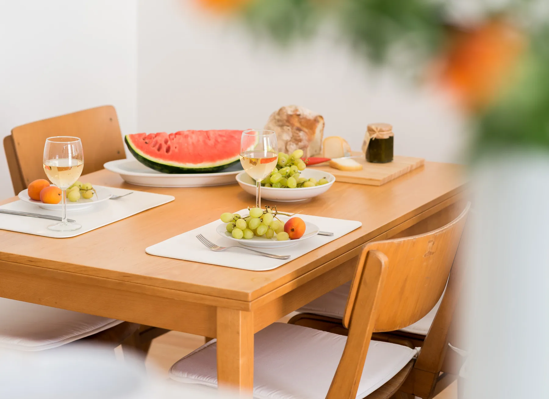 Una mesa de comedor está preparada con fruta, pan y bebidas.