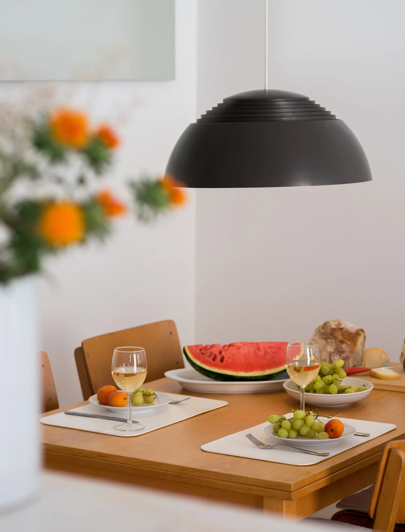 Una mesa de comedor está puesta con fruta y vino bajo una lámpara colgante.