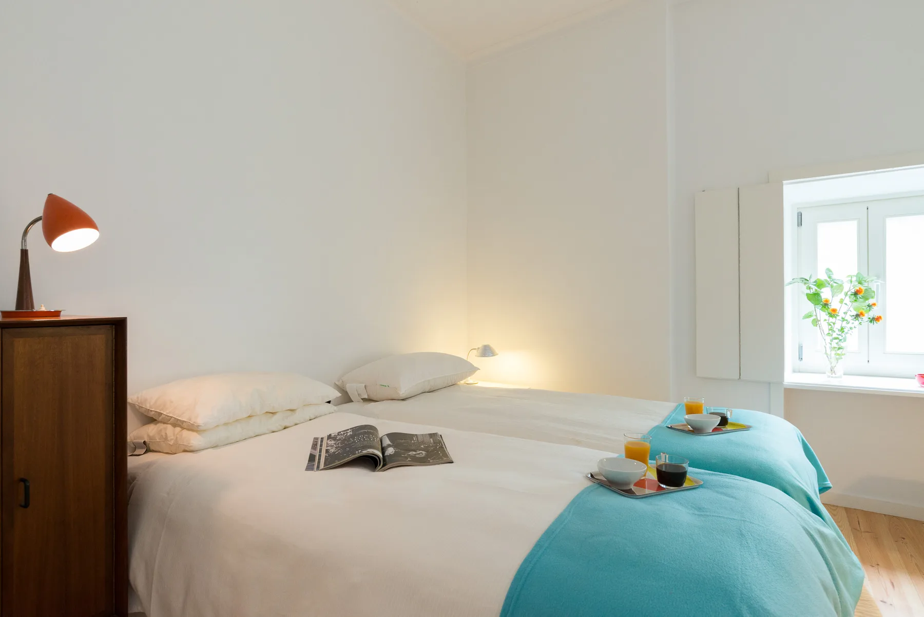 Un dormitorio con una cama tendida y mantas turquesas junto a una ventana.