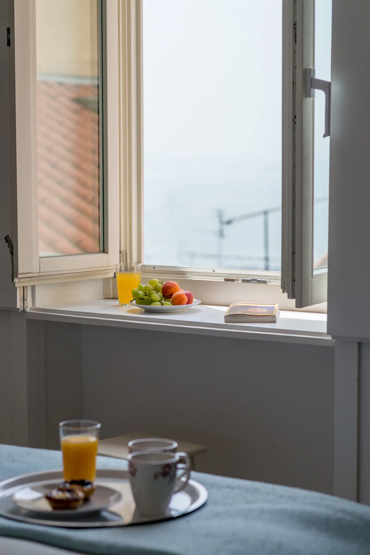 Una ventana abierta da al agua, con fruta y una bebida en el alféizar.