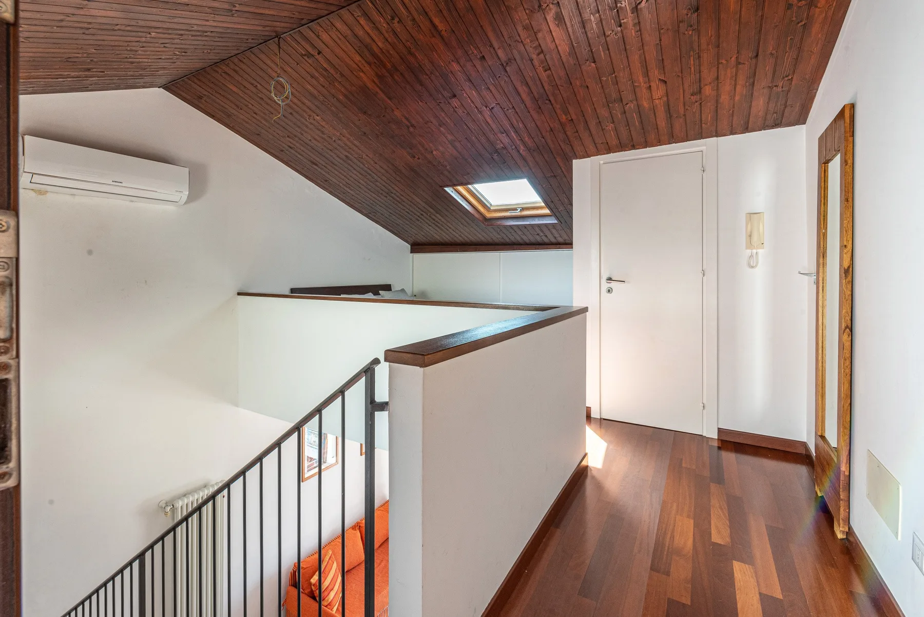Un rellano en la planta superior con una escalera, una puerta cerrada y un techo inclinado de madera.