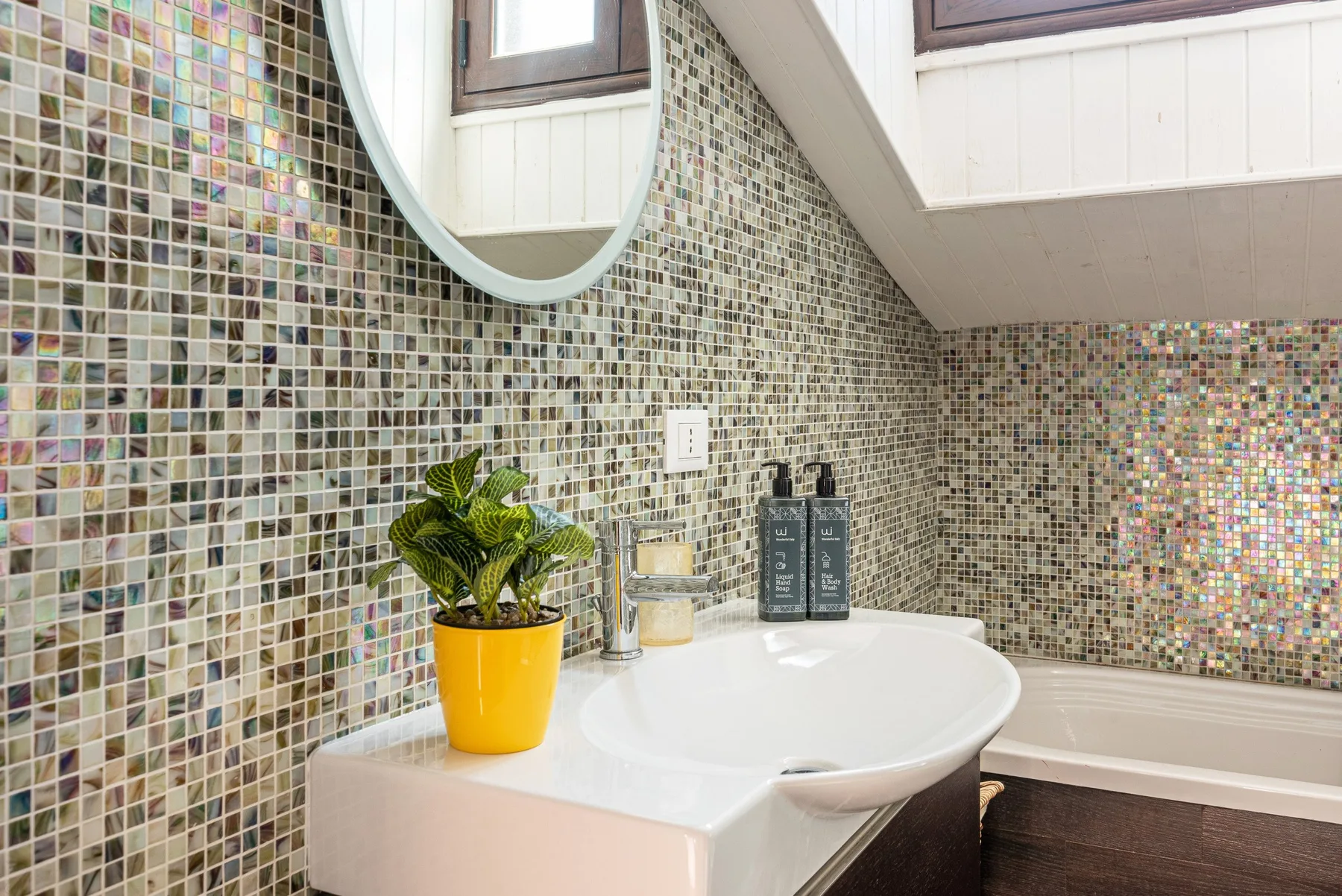 Un lavabo de baño revestido de azulejos, con una pila blanca y una pequeña planta en maceta.