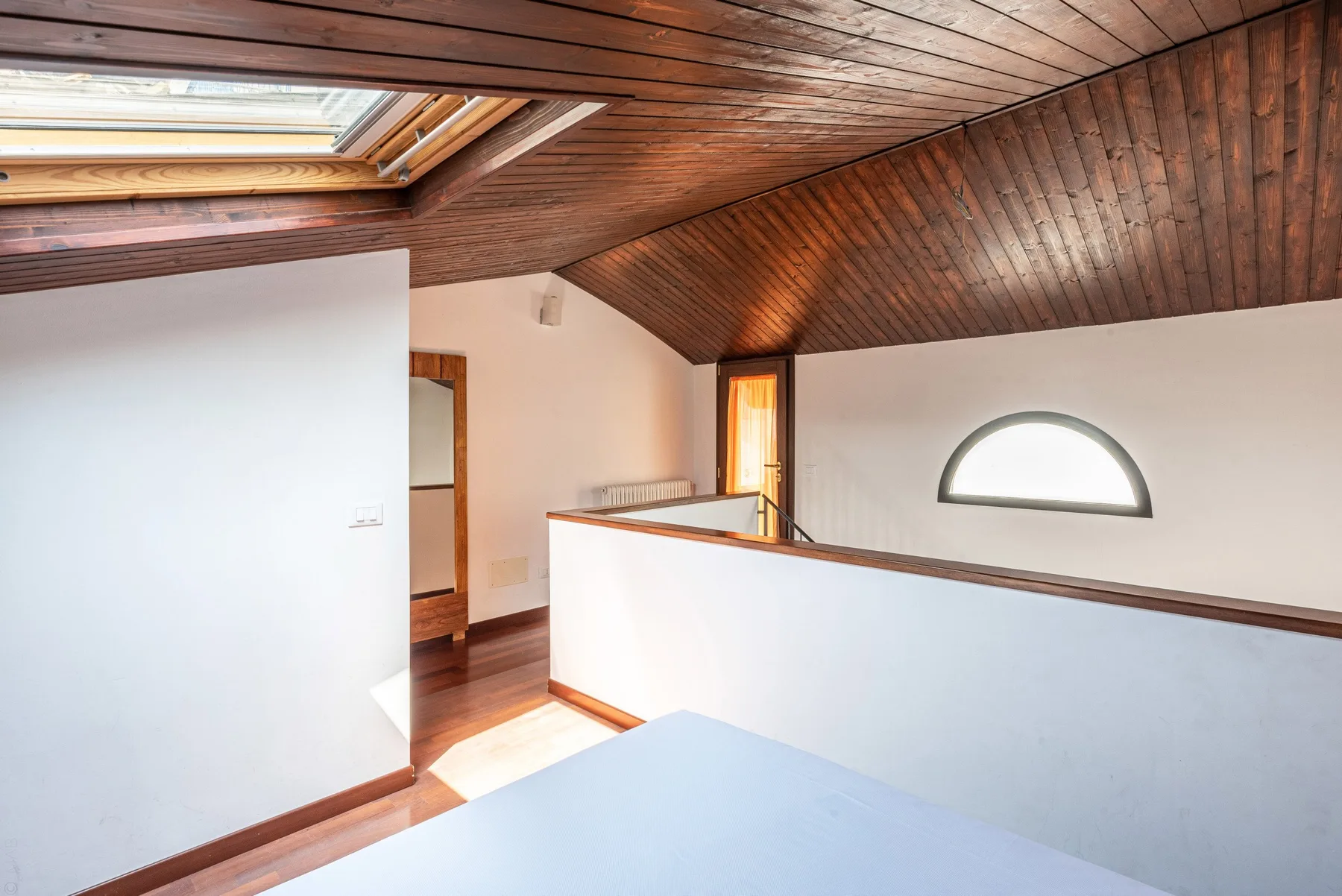 Un luminoso espacio abuhardillado con techo inclinado de madera y un murete.