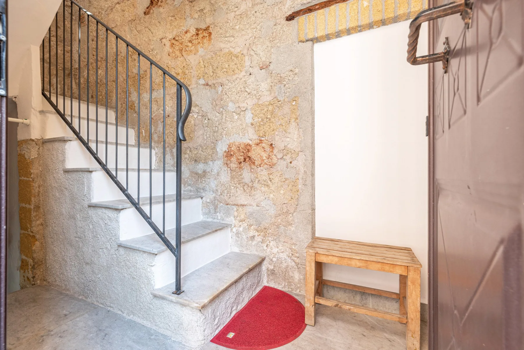 Una escalera de piedra con barandilla oscura junto a una ventana luminosa.