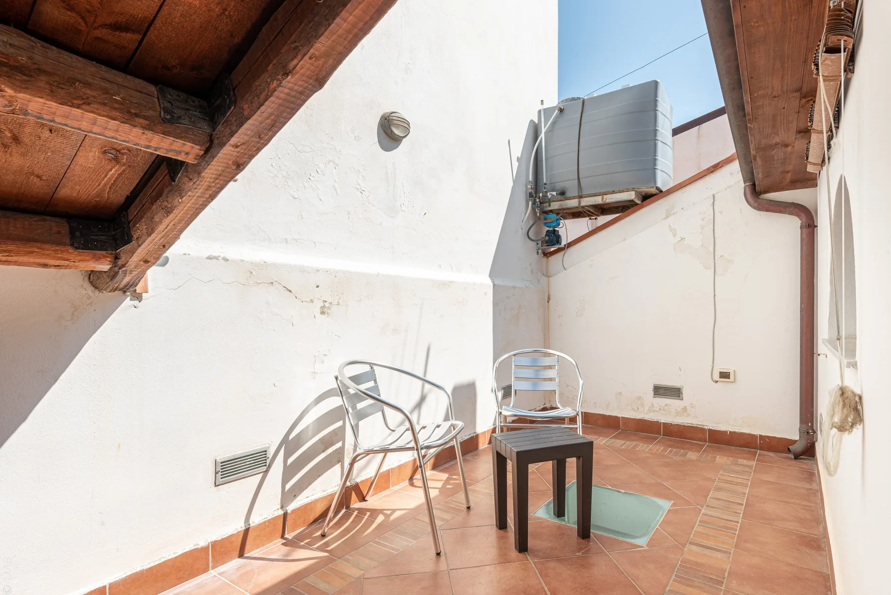 Una pequeña terraza embaldosada con asientos metálicos y un depósito de agua elevado.