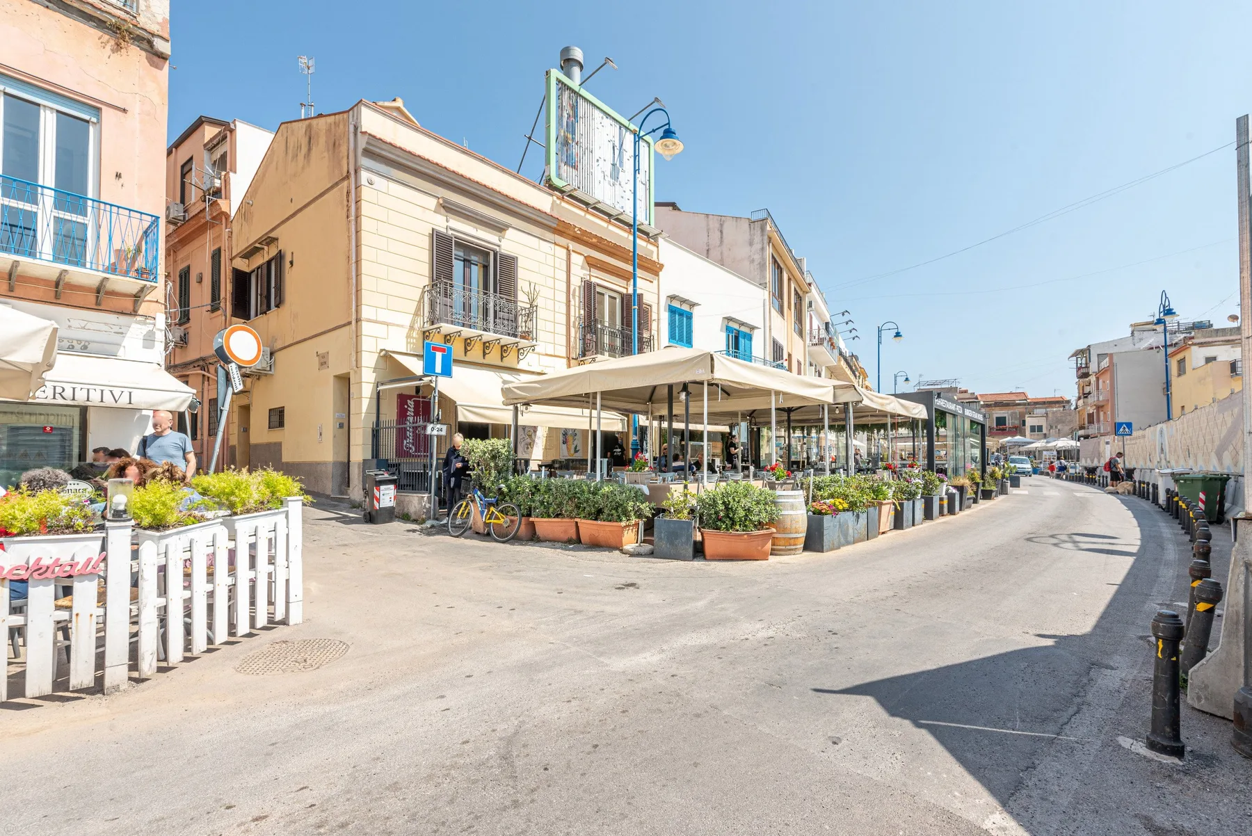 Una esquina soleada con una terraza de café bajo toldos claros.