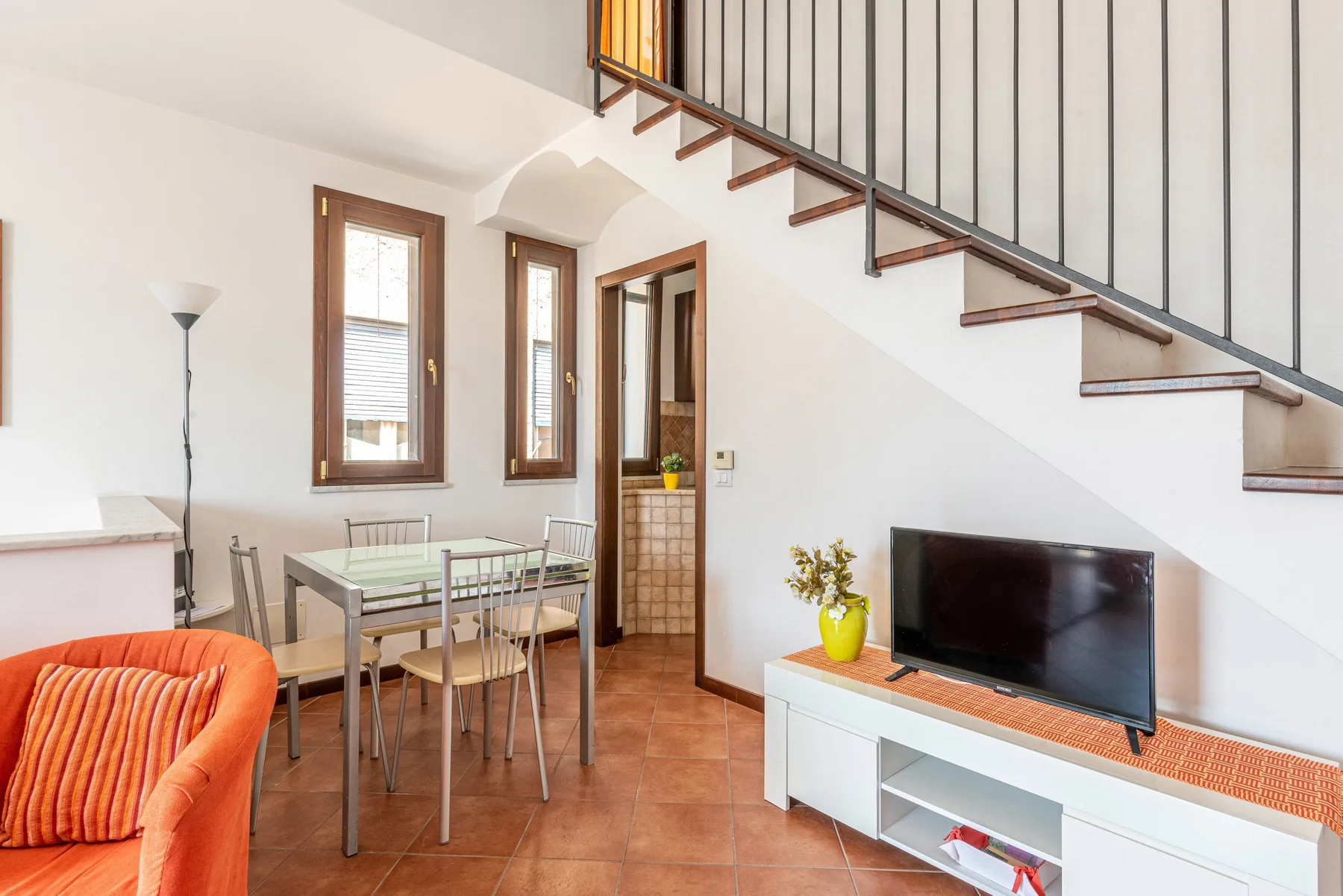 Una luminosa sala de estar y comedor bajo una escalera, con un televisor y una mesa.