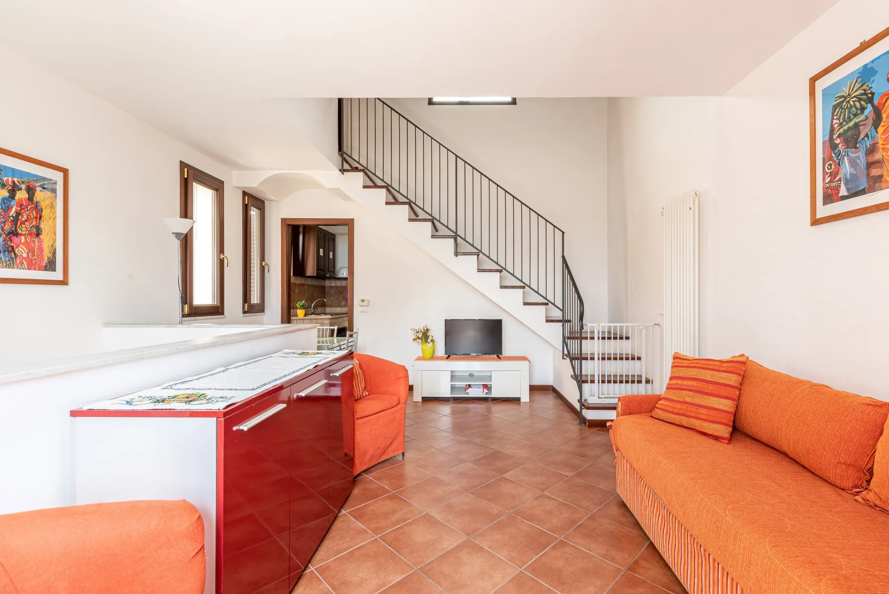 Una sala de estar con asientos naranjas y una escalera junto a la pared del fondo.
