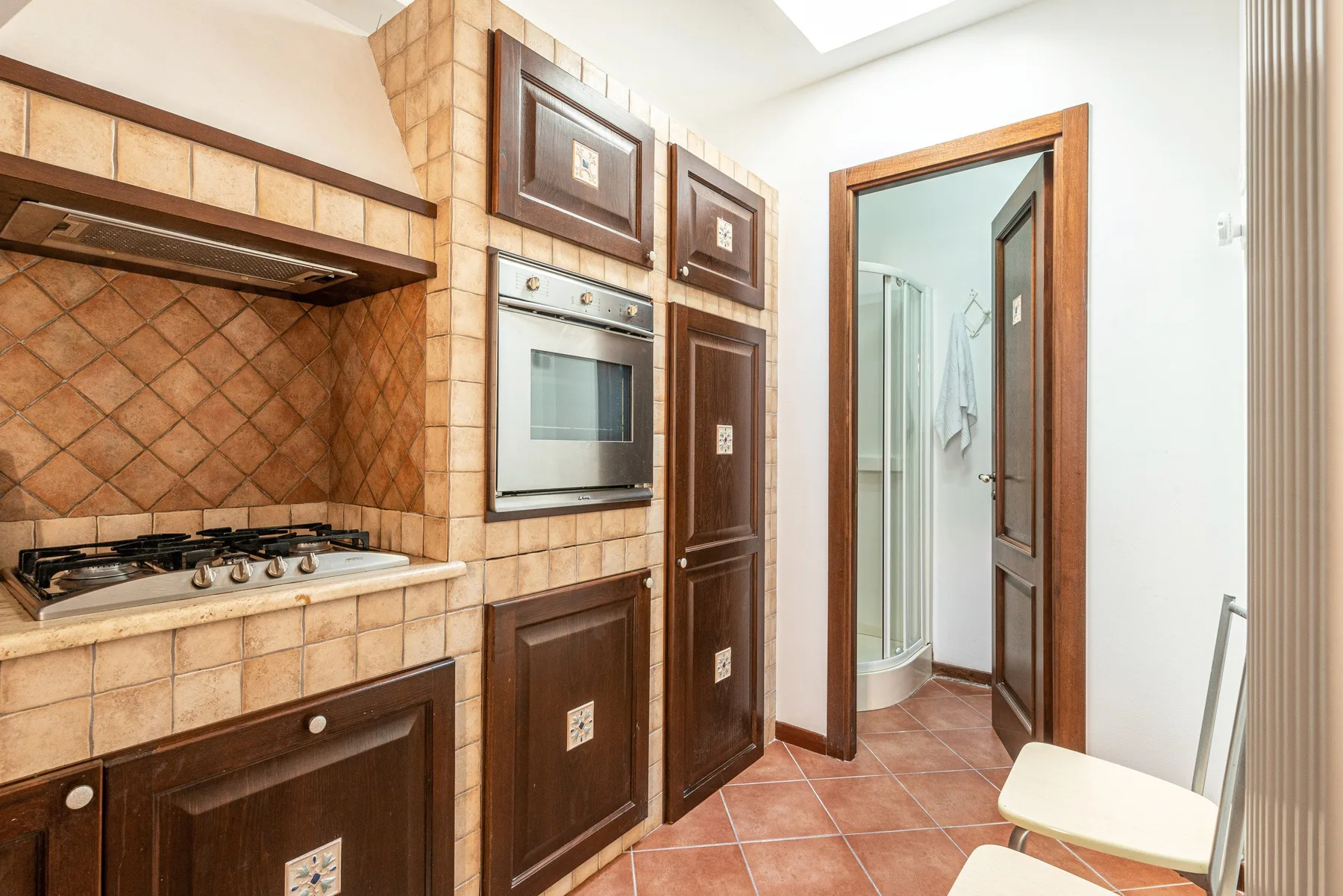 Una cocina con azulejos, electrodomésticos empotrados y una puerta hacia una ducha.