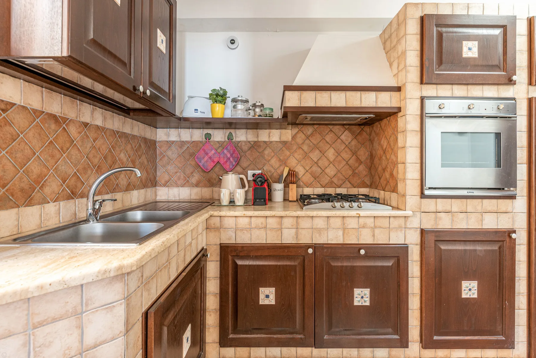 Una cocina alicatada con muebles de madera, un fregadero y un horno integrado.