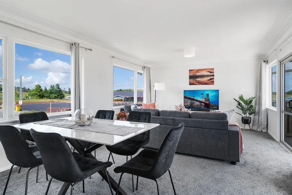 Sala de estar y comedor con una mesa y asientos junto a grandes ventanas.