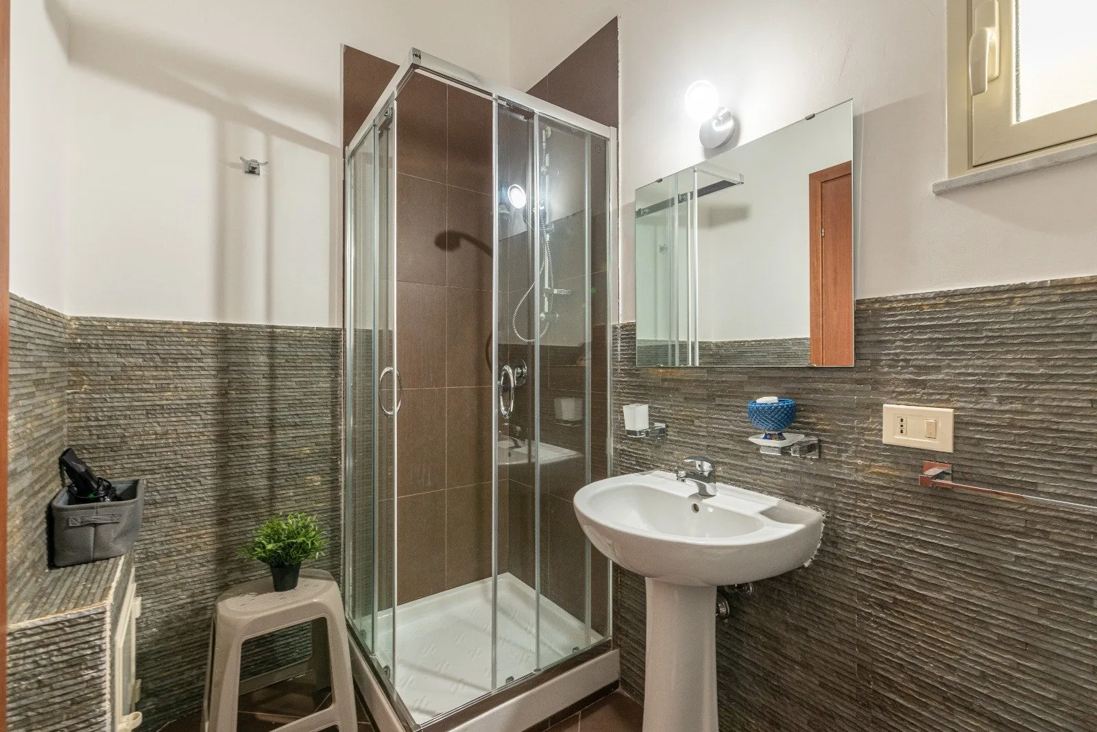 A bathroom with a glass shower, sink, and wall mirror.