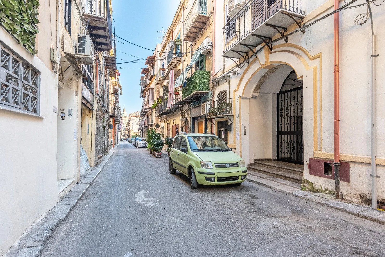 A narrow city street lined with buildings, with a green car parked beside the sidewalk.