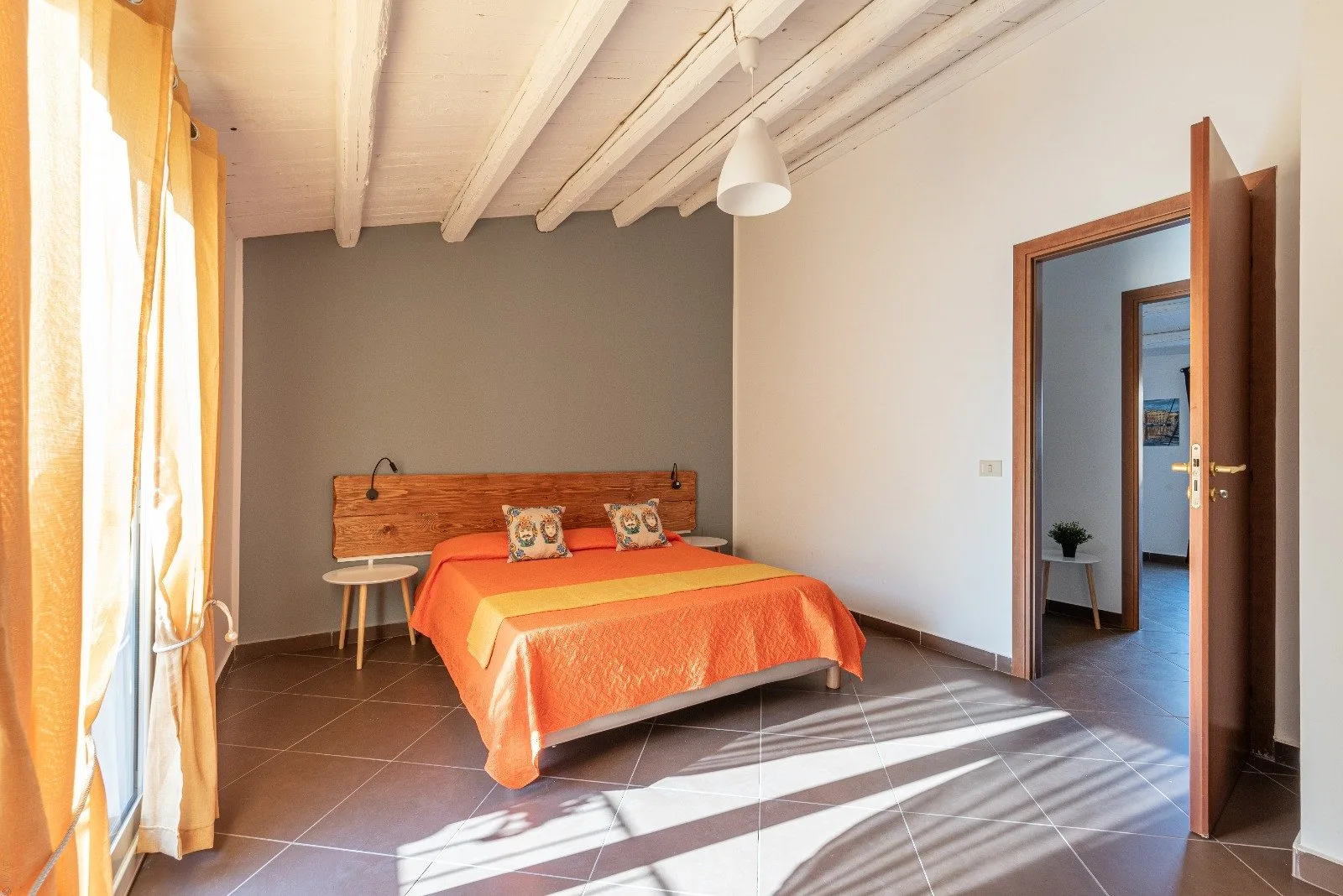 A bedroom with a bed, a small side table, and sunlight streaming through the window.
