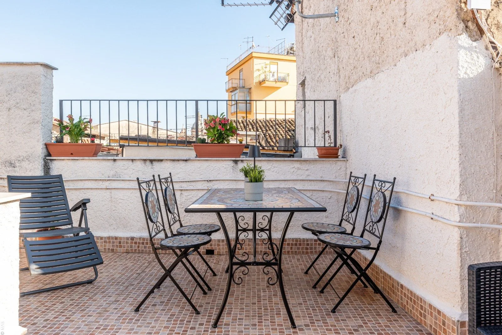 A tiled outdoor terrace with a metal dining table, chairs, and potted plants.