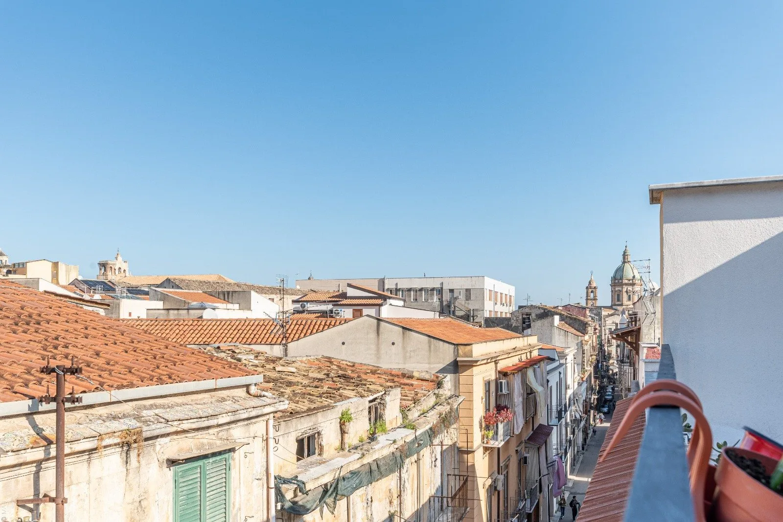 A sunlit city street lined with low-rise buildings and terracotta rooftops.